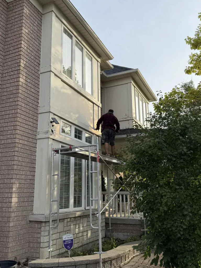 Stucco specialist working from scaffolding on a two-storey front bay